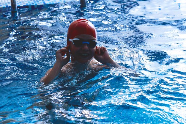 Un alegre nadador sonriente con gorra y Goggles aprende a nadar profesionalmente en la piscina del gimnasio de cerca