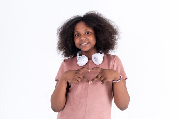 Alegre niña afroamericana preadolescente con cabello rizado que muestra el signo del dedo en forma de corazón