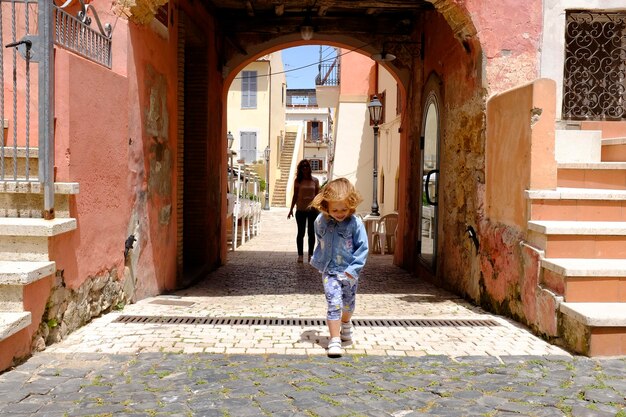 Alegre de la niña corriendo por la acera con la madre en la ciudad