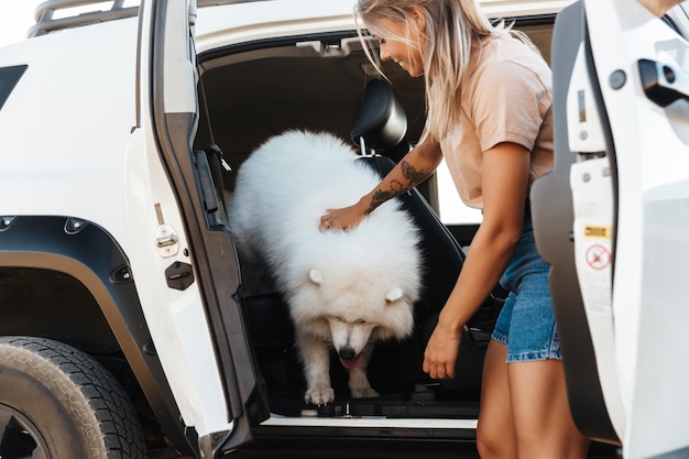 Alegre niña encantadora jugando con su perro mientras está de pie en su coche en la playa.