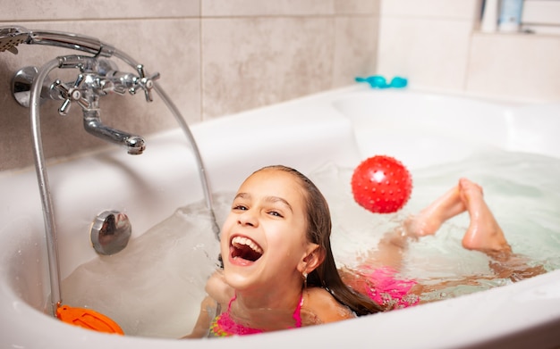 Alegre niña encantadora sonriente se baña con bola roja y mira a la cámara