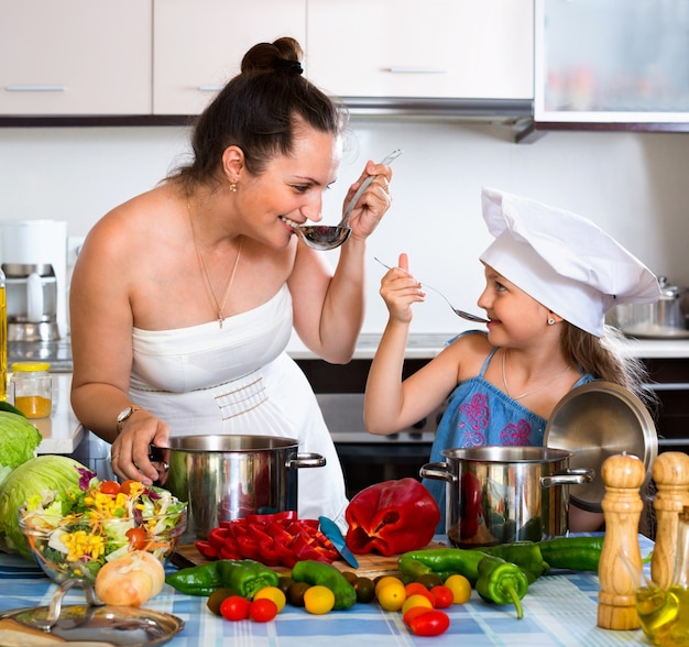 Alegre niña feliz ayudando a la madre a cocinar