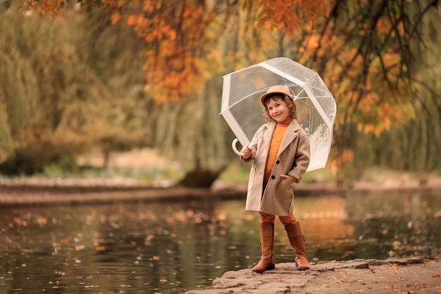 Alegre niña feliz con un paraguas transparente en un paseo en el otoño por el lago