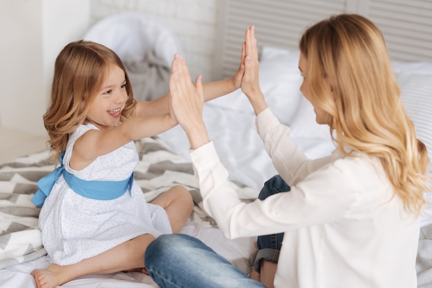 Alegre niña sonriente presionando sus palmas contra las palmas de su madre, jugando con ella un juego de palmaditas para los niños.