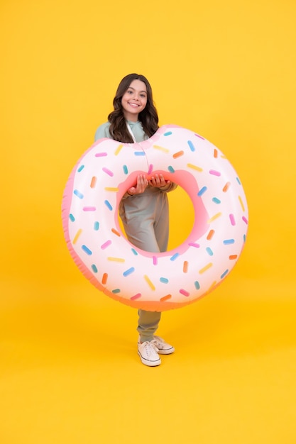 Alegre niño de playa en chándal con anillo de goma de donut para divertirse en la piscina en las vacaciones de verano en verano de fondo amarillo