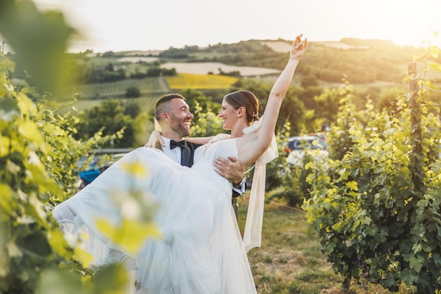 Alegre noivo carregando e girando sua noiva enquanto desfruta na vinha no dia do casamento.