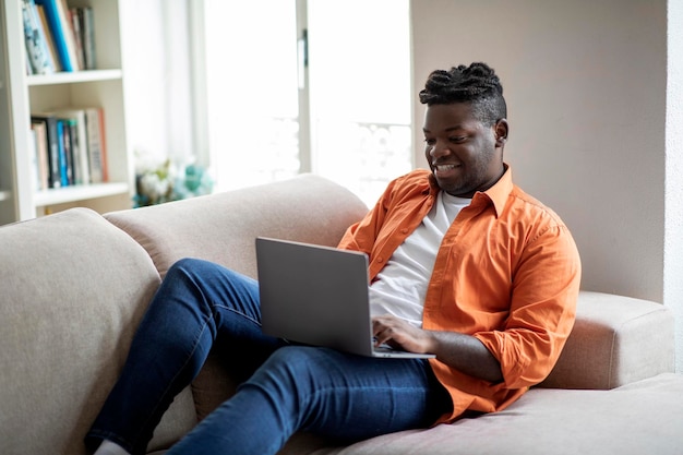 Alegre nómada digital africano que trabaja desde casa usando una computadora portátil
