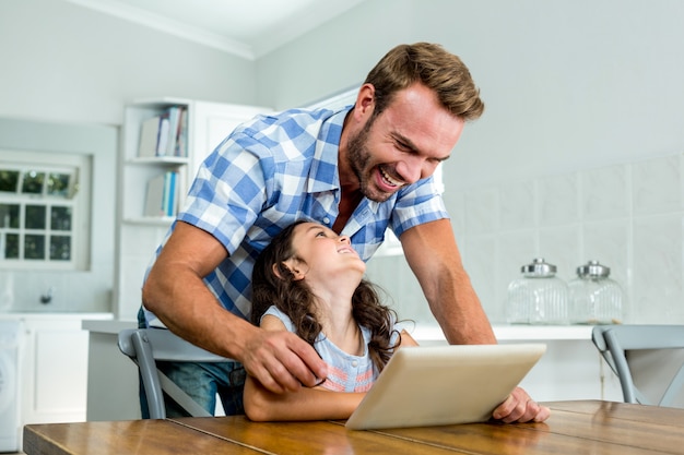 Alegre padre e hija con tableta digital en la mesa