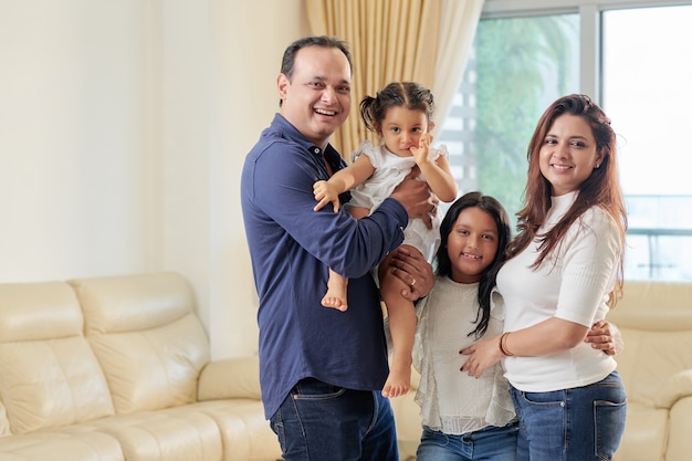 Foto alegre padre indio, madre y dos hijas sonriendo y posando para la foto en su sala de estar