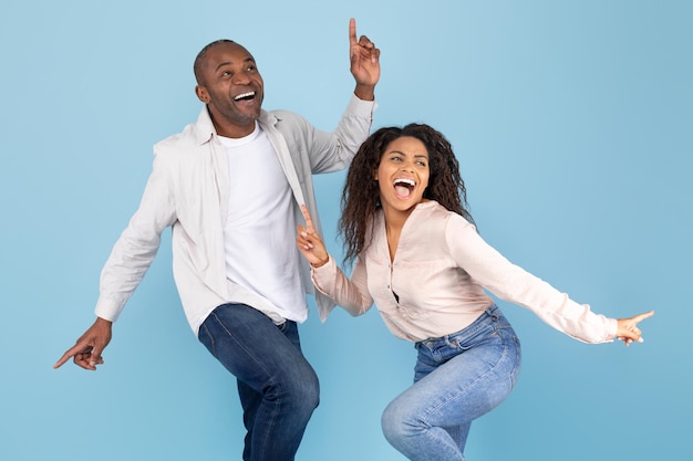 Una alegre pareja afroamericana bailando y sonriendo posando juntos en un estudio azul