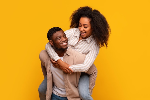 Alegre pareja afroamericana a cuestas con risas en un fondo amarillo