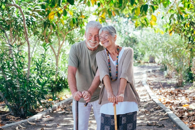 Alegre pareja de ancianos caminando por el bosque con la ayuda de un bastón Sonrientes abuelos ancianos disfrutan de un estilo de vida saludable en un parque público