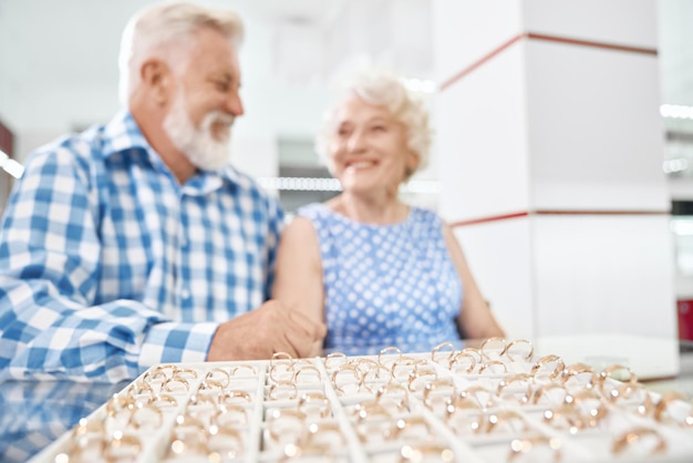 Alegre pareja de ancianos en joyería eligiendo anillos de oro