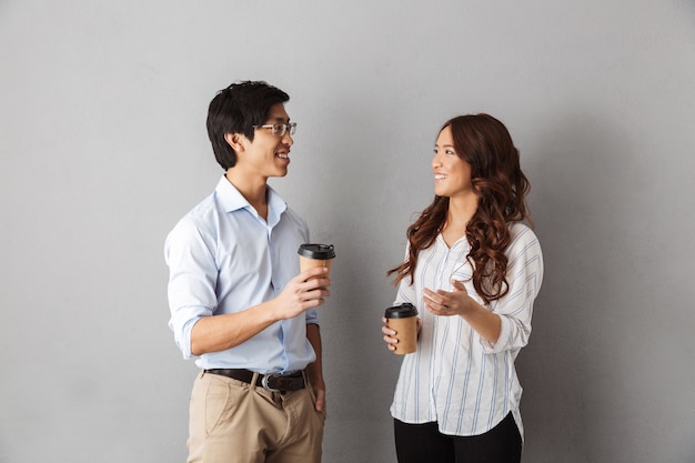 Alegre pareja asiática de pie, hablando, bebiendo café para llevar