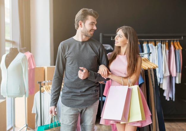 Alegre pareja caucásica con bolsas de compras mirándose, sosteniendo compras en la boutique de ropa