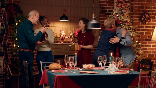 Alegre pareja interracial dando la bienvenida a los invitados a la cena de Navidad en casa. Gente festiva reunida en el comedor para celebrar las vacaciones de invierno con comida casera tradicional.