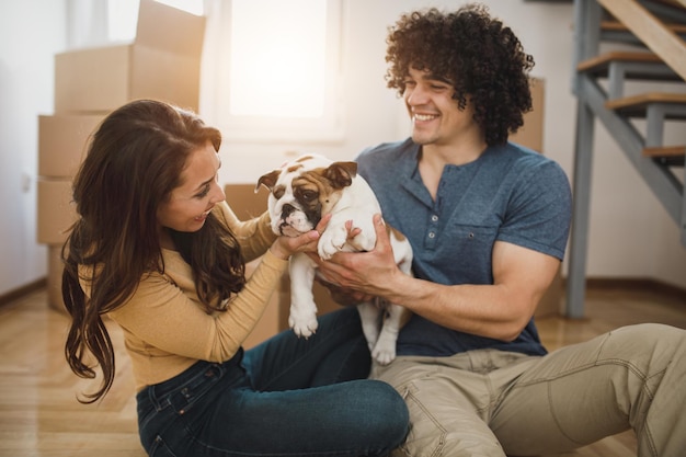 Una alegre pareja joven divirtiéndose con su cachorro de bulldog inglés mientras se muda a su nuevo hogar.