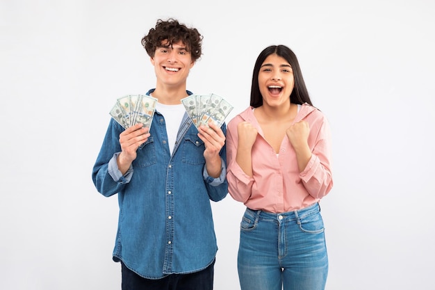 Alegre pareja joven sosteniendo dinero en efectivo celebrando el estudio de la suerte financiera