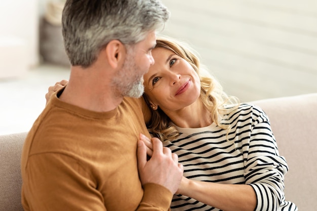 Alegre pareja de mediana edad abrazando sentado en el sofá en casa