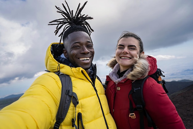 Alegre pareja multiétnica de jóvenes selfie en la cima del concepto de turismo de montaña y pasión por los viajes