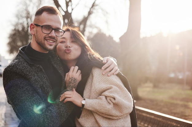 Alegre pareja multirracial abrazándose al aire libre en la ciudad. Chica asiática con su novio caucásico.