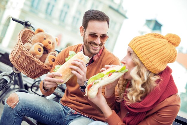 Alegre pareja romántica al aire libre disfrutando de sándwiches