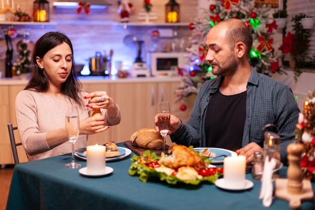 Alegre pareja romántica comiendo la cena de Navidad sentado en la mesa de comedor