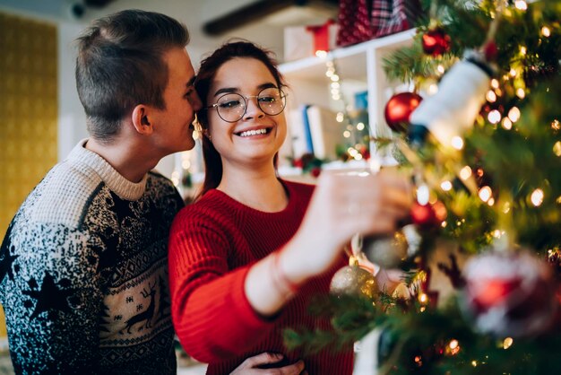 Alegre pareja romántica decorando el árbol de Navidad en casa