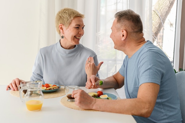 Alegre pareja senior saludable desayunando juntos sonriendo y riendo