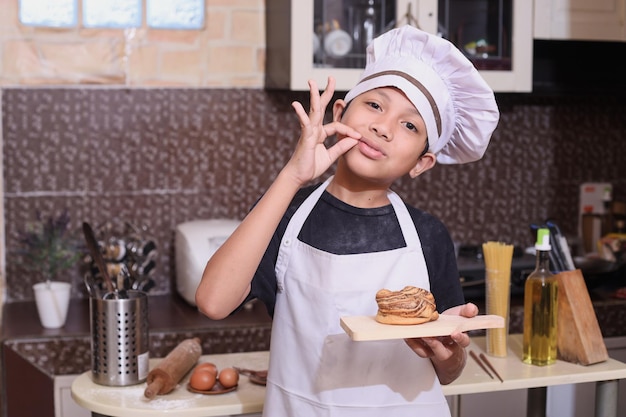 Alegre pequeno chef mostrando bom gosto enquanto segura pão assado na cozinha