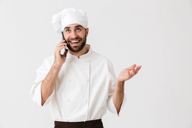 alegre positivo jovem chef posando de uniforme, falando pelo celular.