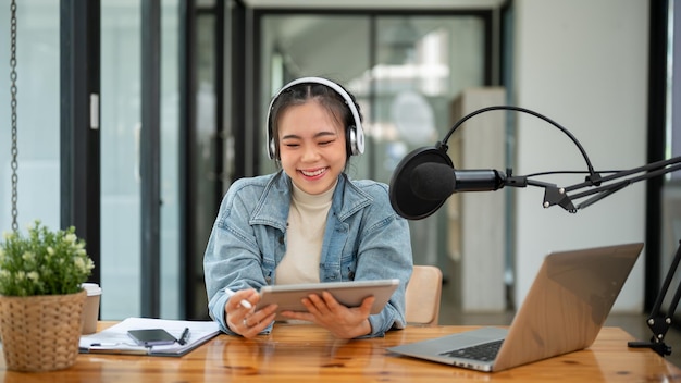Una alegre presentadora de radio asiática hablando en un micrófono y grabando su podcast