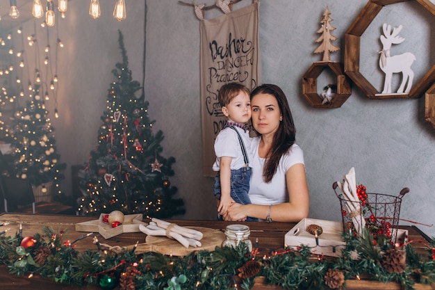 Alegre retrato de Natal de feliz mãe e filho com presentes de ano novo e véspera de Natal com decoração de celebração e luzes de Natal