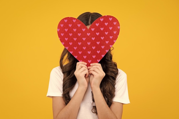 Una alegre y romántica jovencita tiene un corazón rojo símbolo de amor por el día de San Valentín aislado en un fondo amarillo