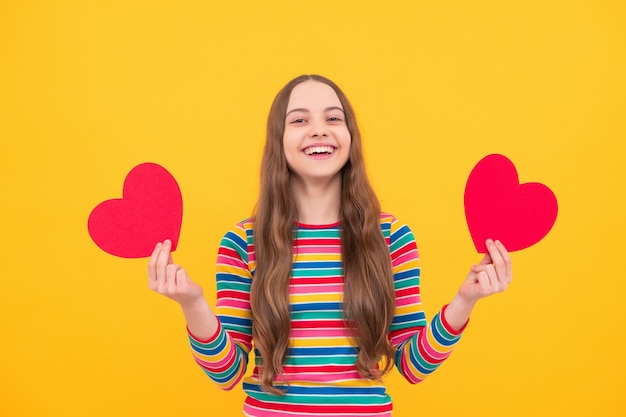 Una alegre y romántica jovencita tiene un corazón rojo símbolo de amor por el día de San Valentín aislado en un fondo amarillo