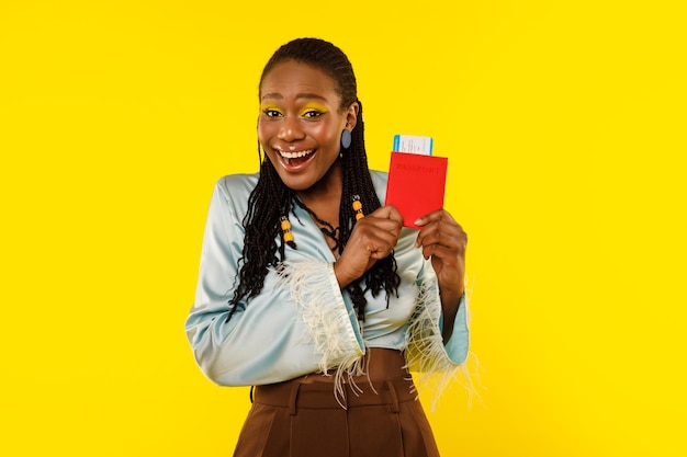 Alegre senhora africana segurando passaporte e ingressos em fundo amarelo