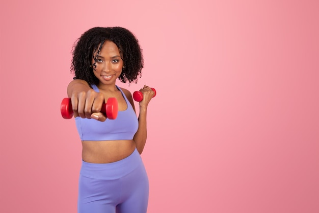 Alegre senhora afro-americana milenar em roupas esportivas gosta de exercícios com halteres de mão