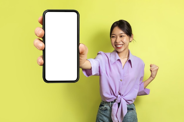 Alegre senhora japonesa mostrando um telefone enorme gesticulando sim fundo amarelo