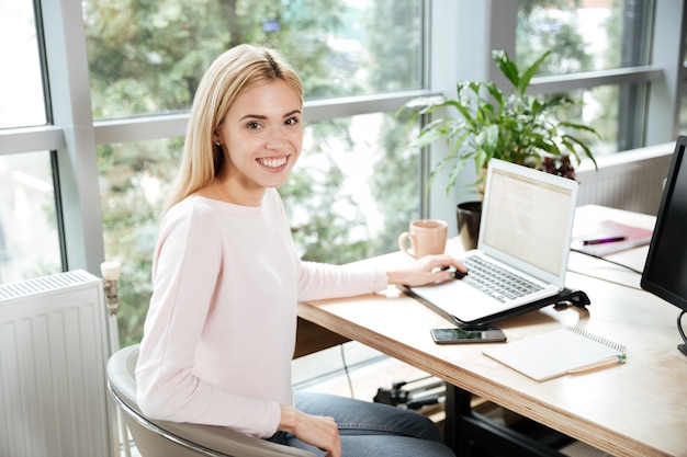 Alegre senhora sentada no escritório coworking usando laptop