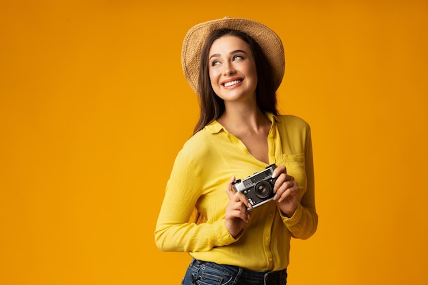 Alegre señora viajera sosteniendo cámara retro posando en el estudio