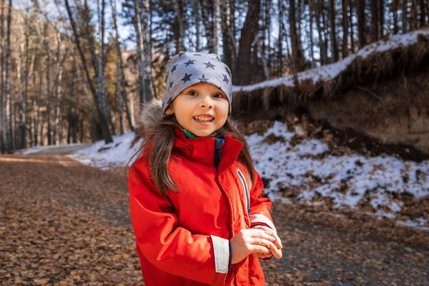 Alegre sonriente feliz niña en edad preescolar en chaqueta roja en el bosque de otoño profundo