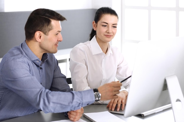 Alegre sonriente hombre de negocios y mujer que trabaja con la computadora en la oficina moderna. Disparo en la cabeza en la reunión o el lugar de trabajo. Trabajo en equipo, asociación y concepto de negocio.