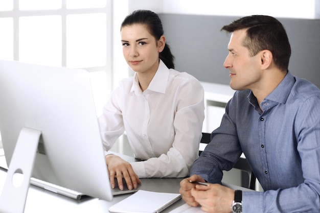 Alegre sonriente hombre de negocios y mujer que trabaja con la computadora en la oficina moderna. Disparo en la cabeza en la reunión o el lugar de trabajo. Trabajo en equipo, asociación y concepto de negocio.