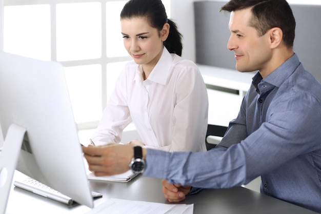 Alegre sonriente hombre de negocios y mujer que trabaja con la computadora en la oficina moderna. Disparo en la cabeza en la reunión o el lugar de trabajo. Trabajo en equipo, asociación y concepto de negocio.