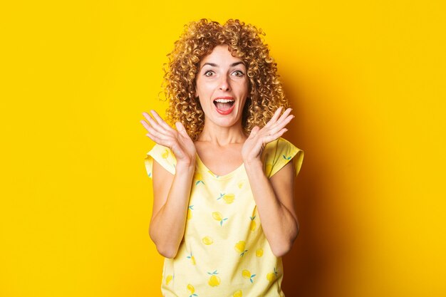 Alegre sorprendida sorprendida joven de pelo rizado sobre un fondo amarillo brillante