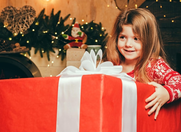 Alegre sorridente e feliz garotinha segurando um presente gigantesco da véspera de Natal do Papai Noel e m