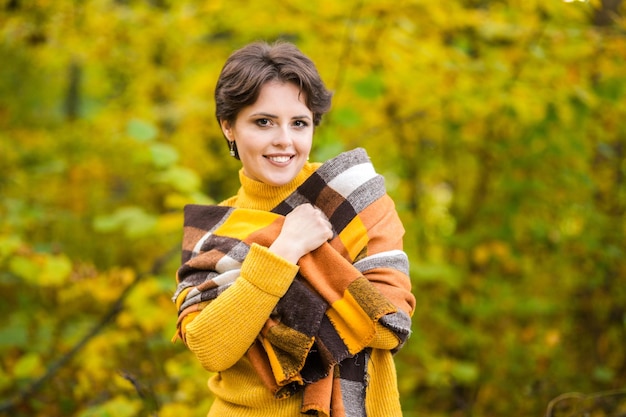 Alegre sorridente jovem morena embrulhada em cobertor na floresta de outono