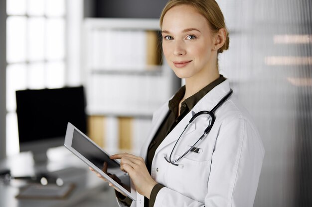 Alegre sorridente médica usando computador tablet na clínica. Retrato de mulher médica amigável no trabalho. Serviço médico perfeito no hospital. Conceito de medicina.