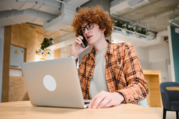 Un alegre trabajador independiente que hace una llamada telefónica comparte buenas noticias sobre el proyecto que trabaja en el interior de un café.