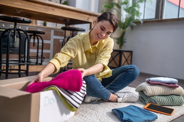 Alegre voluntária feminina embalando roupas para doação